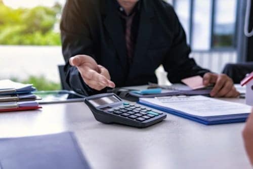 A man and woman discussing the impact of rising fire insurance costs on California campground operators at a desk with a calculator.