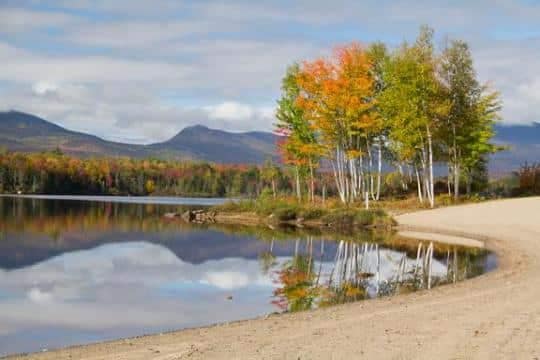 Jericho Mountain State Park in New Hampshire offers a picturesque sandy beach with trees and mountains in the background for visitors to enjoy.