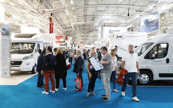 A group of people standing in a room filled with a lot of innovative and exciting RVs, showcasing the future of caravanning at Paris' Salon des Vehicules De Loisirs