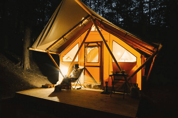 A Huttopia Campground tent is lit up in the woods at night in Southern Maine.