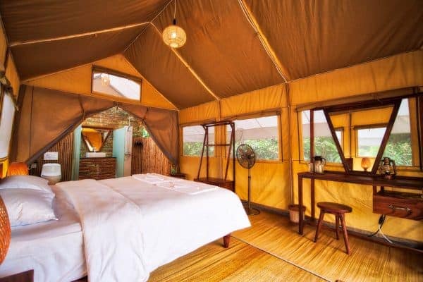 A bedroom in a safari-style tent with a bed and a bedside table.