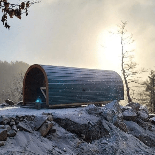 A small cabin nestled in the Éco-Odyssée Nature Park, surrounded by a snowy hill.