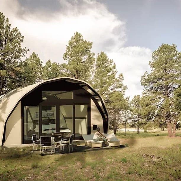 A luxurious white tent sits in the middle of a wooded area, offering a glamping experience at an eco-resort.