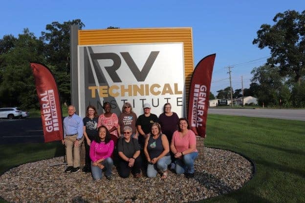 A group of All-Female Tech Class Graduates standing in front of a sign that says RV Technical Live.
