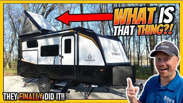 A man is standing next to an Ember RV with a rooftop tent system.