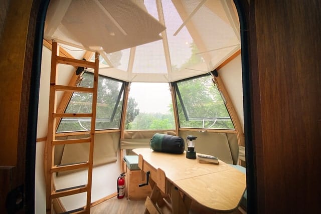 The inside of a tiny house, designed as one of Ontario Teardrop Camping Pods, with a ladder and a table.