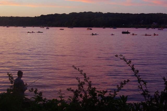 A man is fishing in a lake at sunset at a campground.