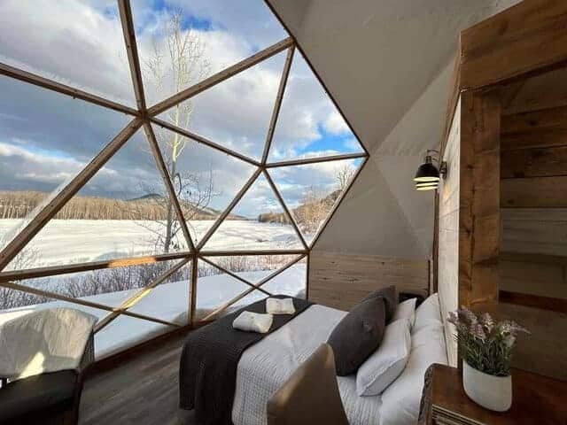An igloo with a bed and a view of the snow, perfect for a unique glamping experience.