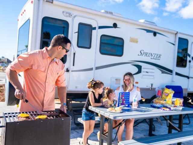 A family sits at a picnic table in front of an rv, enjoying the lavish amenities of Camp Margaritaville RV Resort Auburndale.