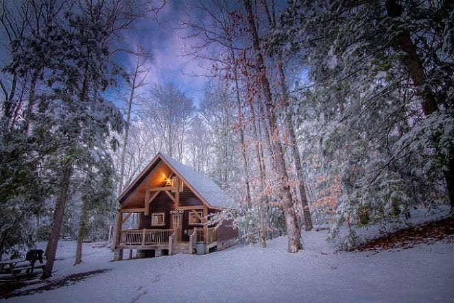 An Affordable cabin in the woods covered in snow for Winter Escapes.