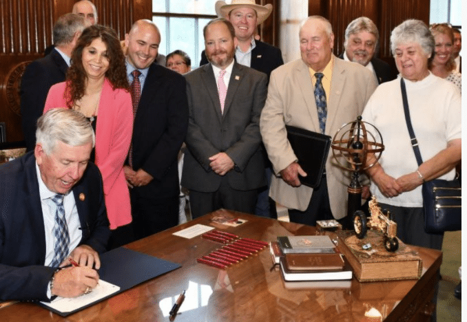 A group of people standing around a table signing a document, symbolizing industry unity.