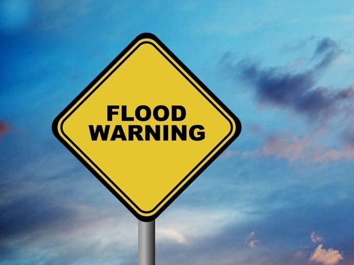 A yellow and black flood warning sign amidst the potential of Evacuations, against a cloudy sky.
