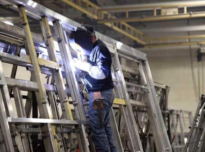 An American welder is working on a frame in a factory while capturing footage for factory tour videos.