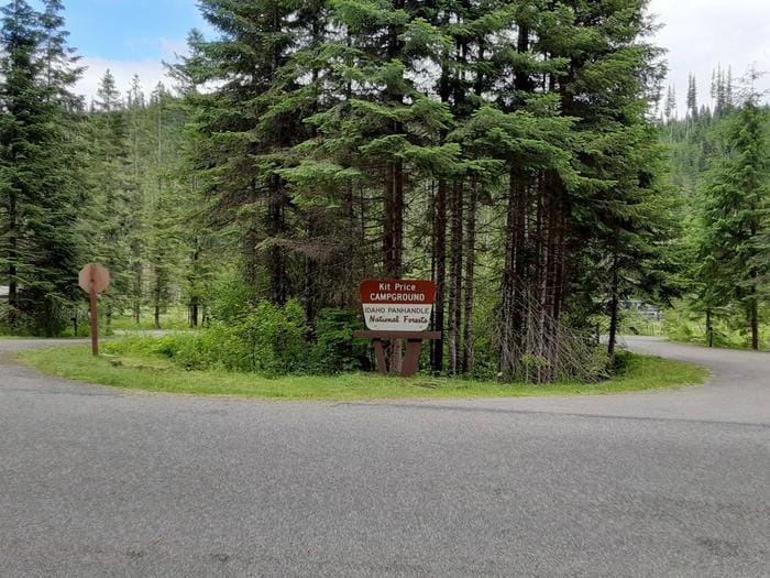 A sign in the middle of a forest with trees in the background, announcing the reopening of Kit Price Campground just in time for Memorial Day Weekend.