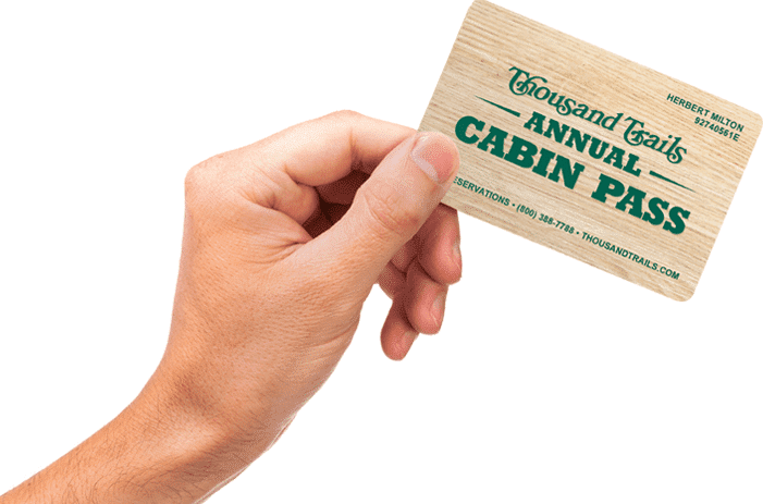 A person proudly displaying a wooden card with the phrase "Cabin Pass" engraved on it, signifying their exclusive membership to Thousand Trails.