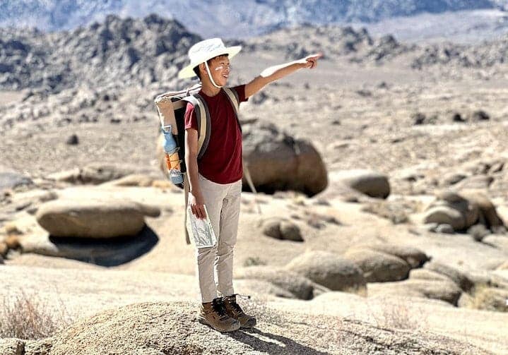 A girl with a backpack is standing on a rock in the desert, enjoying a serene environment away from the usual kids and RVshare craze.