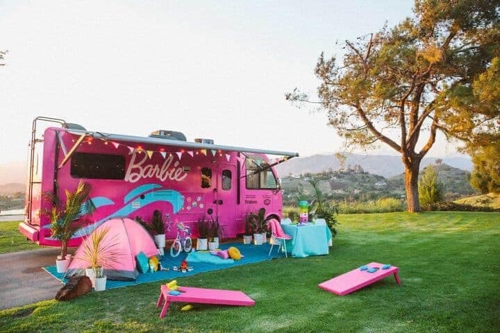 A Barbie RV, painted in vibrant pink, is peacefully parked in the lush green grass.