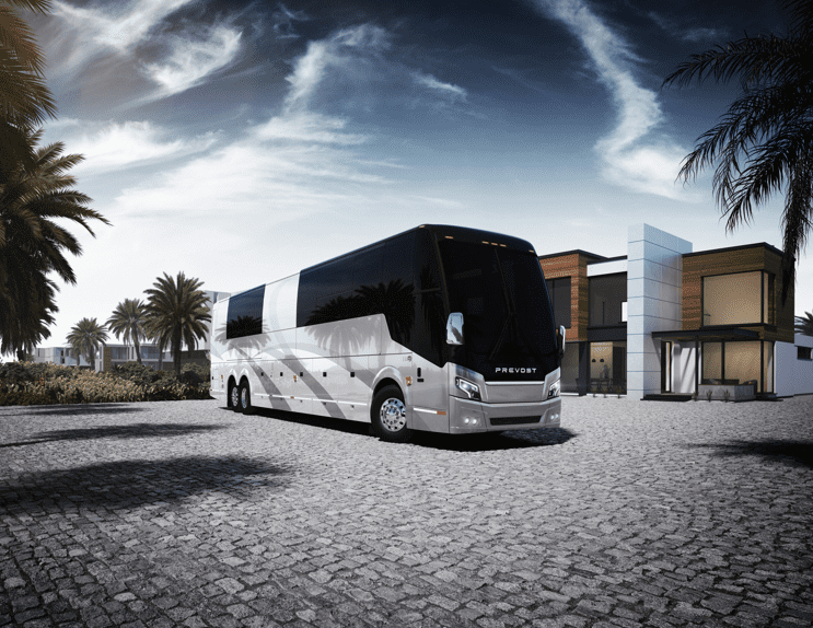 A white Prevost tour bus parked in front of a palm tree.