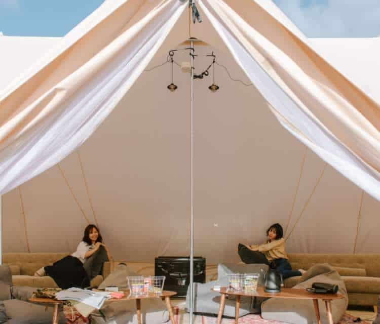 Two women enjoying luxury coastal glamping in Japan with breathtaking ocean views from inside their tent.