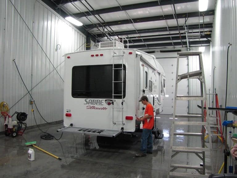 A man is cleaning a Sabre Fifth Wheels RV in a garage.