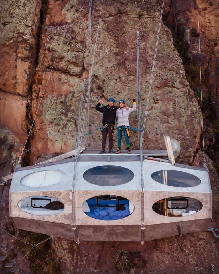 Two men standing on top of a Sky Lodge on a cliff.