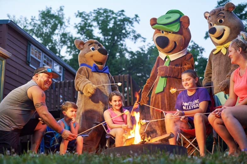 A group of people sitting around a campfire at Yogi Bear's Jellystone Park in Kentucky, with bear mascots.