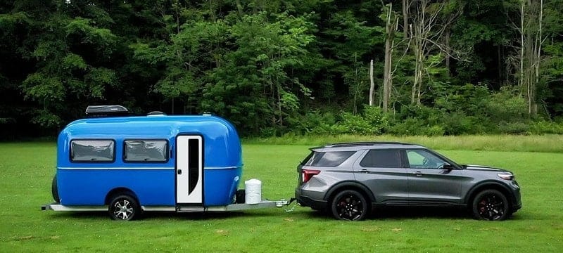 Cortes Campers expands business in Wyoming with a blue SUV towing a camper trailer.