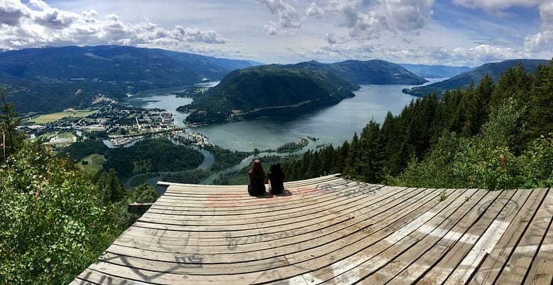 Two people sitting on a wooden platform overlooking a lake at the Sicamous KOA campground.