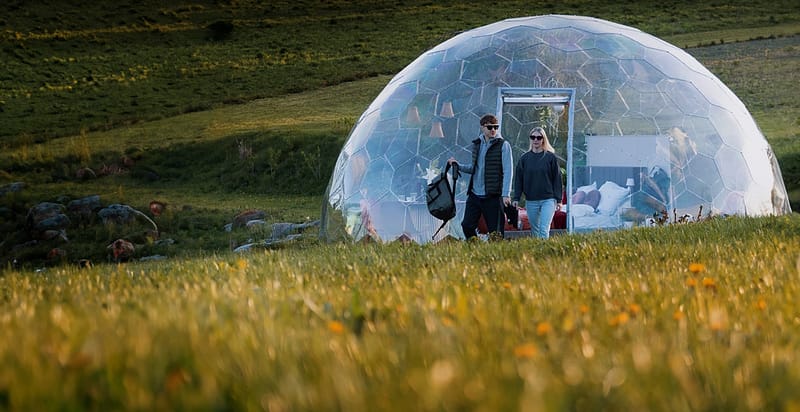 Two people walking towards a luxurious Hypedome in a green field during a sunny day.