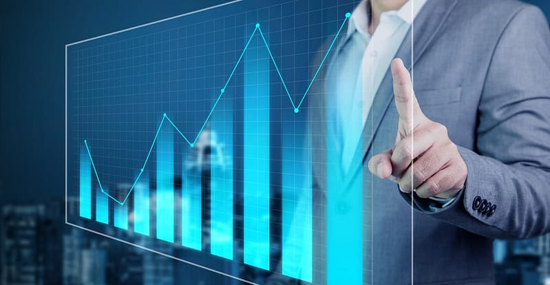 A businessman is pointing at a graph on a screen.