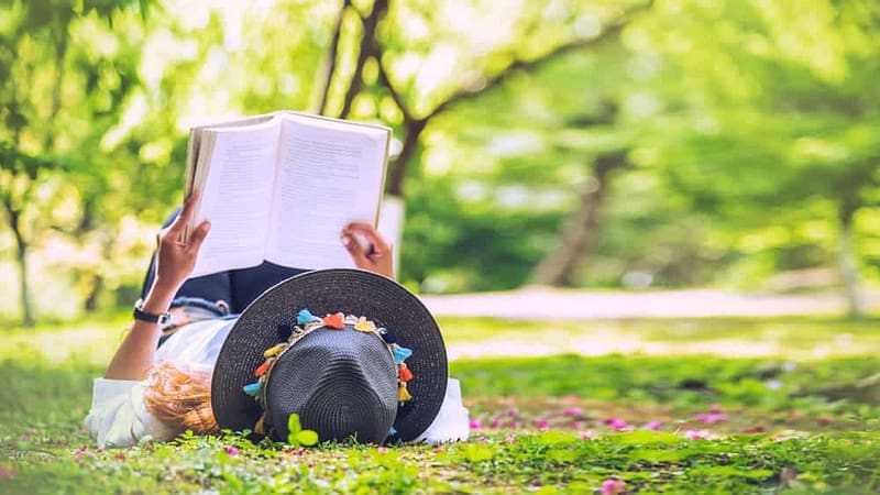 A woman relaxing on the grass, engrossed in a captivating book at a Kansas State Park.