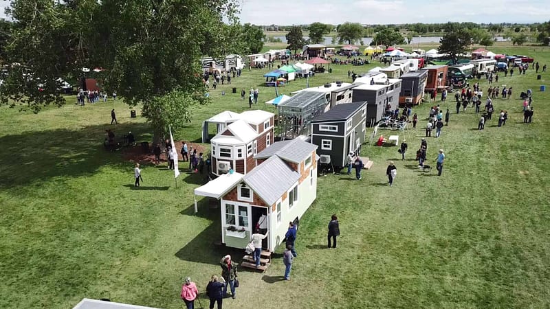 An aerial view of a crowd of people at the Colorado Tiny House Festival, featuring unique RVs and tiny homes.