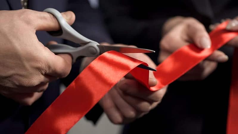 Two people participating in a Ribbon-Cutting Ceremony by cutting a red ribbon with scissors at an RV Inn Style Resort.