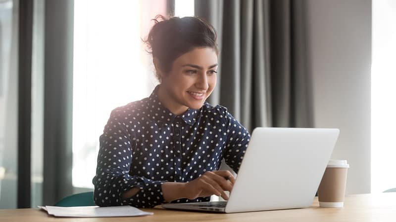 A smiling woman using a laptop in an office, staying informed with TACO Webinars.