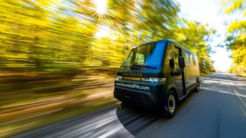 A G2 electric RV van driving down a road with trees in the background.