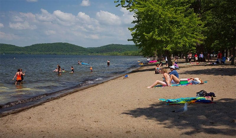 A group of people on a sandy beach at Sand Bar State Park, which has recently been honored with the Park of the Year Award in Northwest Vermont.