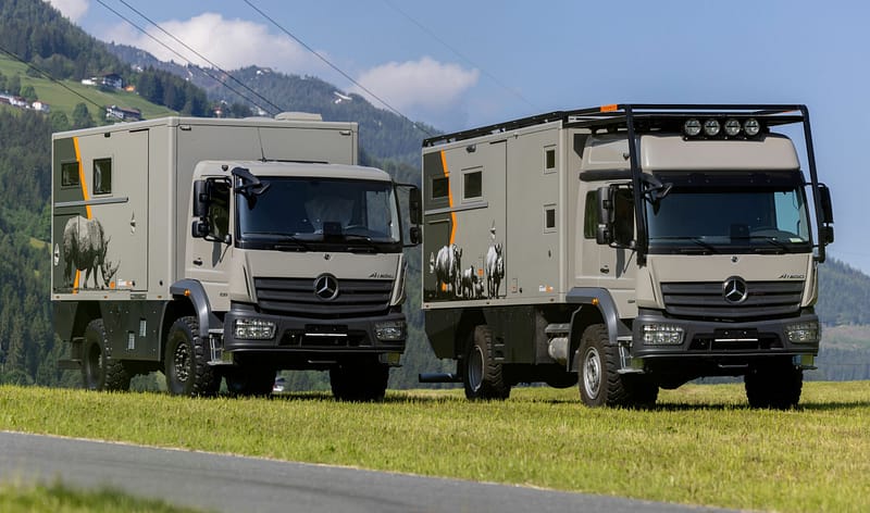 Two Mercedes Benz trucks, serving as adventure vehicles for outdoor adventurers, parked on the side of a road.