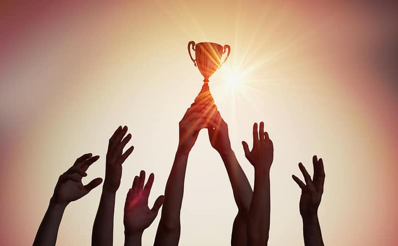 A group of people reaching for the Major Tourism Award trophy at Julia Creek Caravan Park.