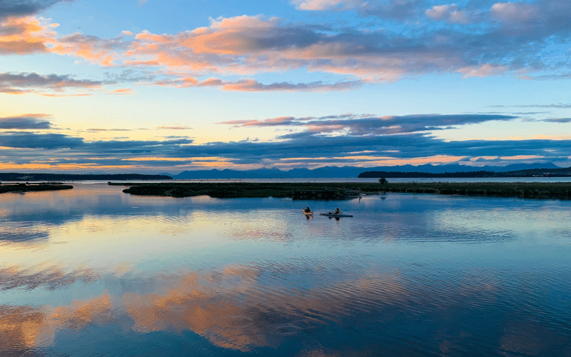 A man is paddling a canoe in a lake at sunset near the Living Forest Oceanside Campground in British Columbia.