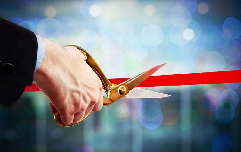 A person cutting a red ribbon with a pair of scissors.