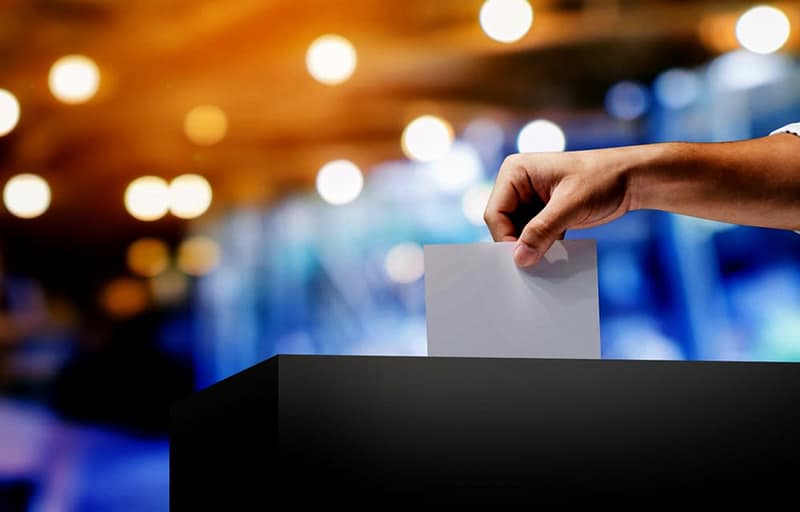 A person putting a paper into a voting box.