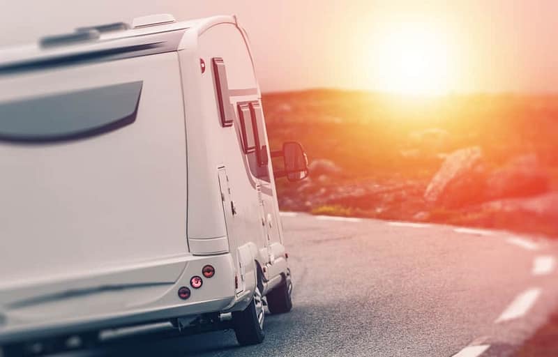 A white RV is driving down a road at sunset.