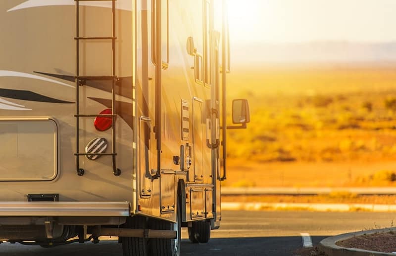An RV, equipped with Lippert's Road Defense technology, gracefully cruises down a desert road with its durable powder coating ensuring ultimate protection against harsh terrain.