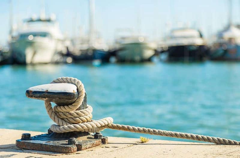 A rope tied to a dock with boats in the background.