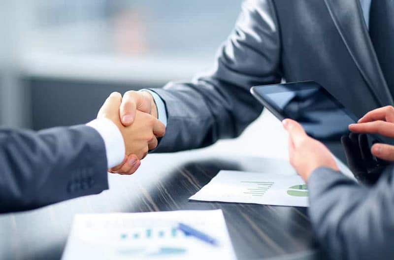 Two business people representing Pathfinder Ventures and Agassiz Expansion shaking hands at a table during a property acquisition agreement.