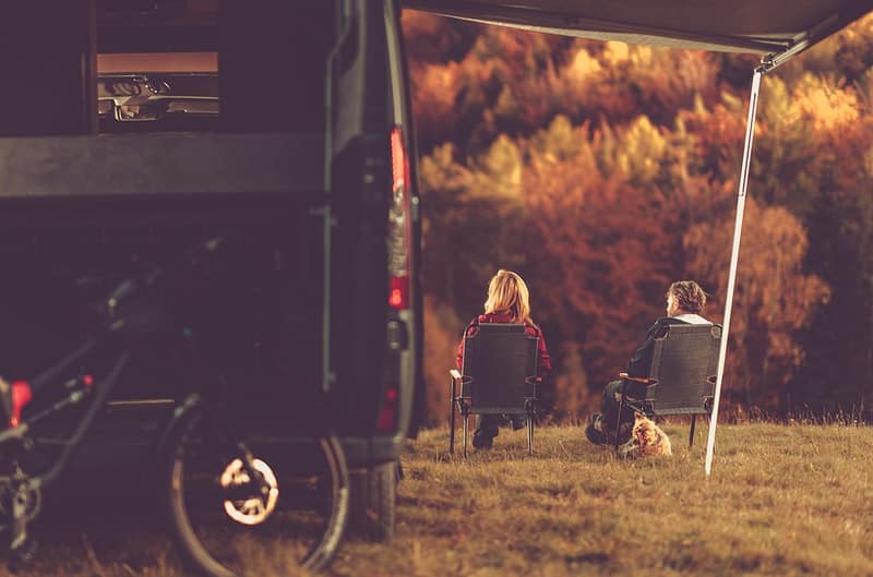Two people sitting in front of a camper, enjoying the outdoors as part of REI's #OptOutside Campaign.