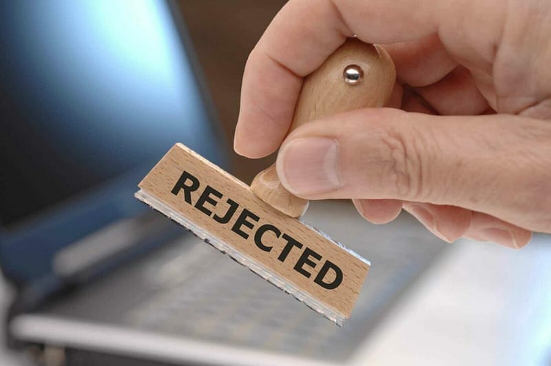 A person holding a wooden stamp with the word rejected in front of a laptop during development.