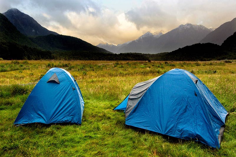 Two tents set up in a grassy field with mountains in the background, reminding campers of Auckland Council's freedom camping regulations.