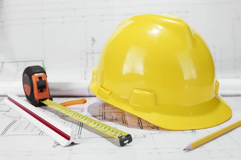 A yellow hard hat sits on top of blueprints for a construction project.