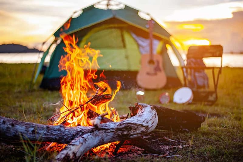 A campfire near a tent and a guitar at a Q2 KOA camping site.